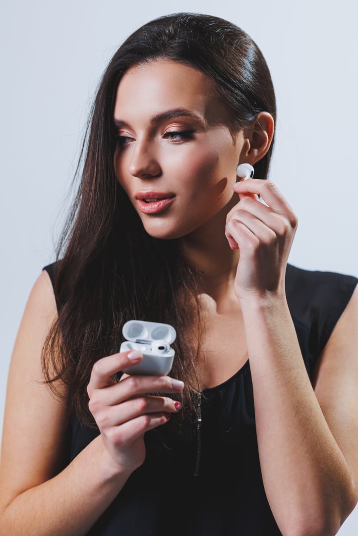 A woman puts wireless headphones into her ears. Female hands hold two white glossy wireless Bluetooth headphones.